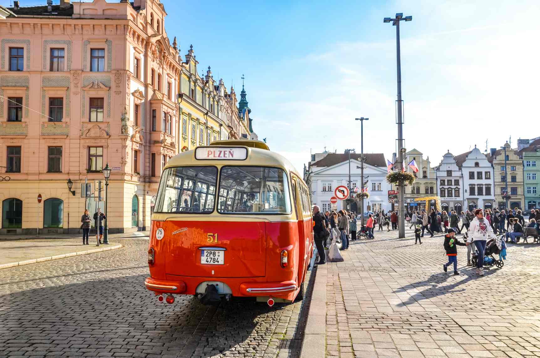 Vintage red and cream tram displaying “Plzen” in the historic center of Pilsen, Czech Republic, surrounded by colorful European buildings and a lively cobblestone square