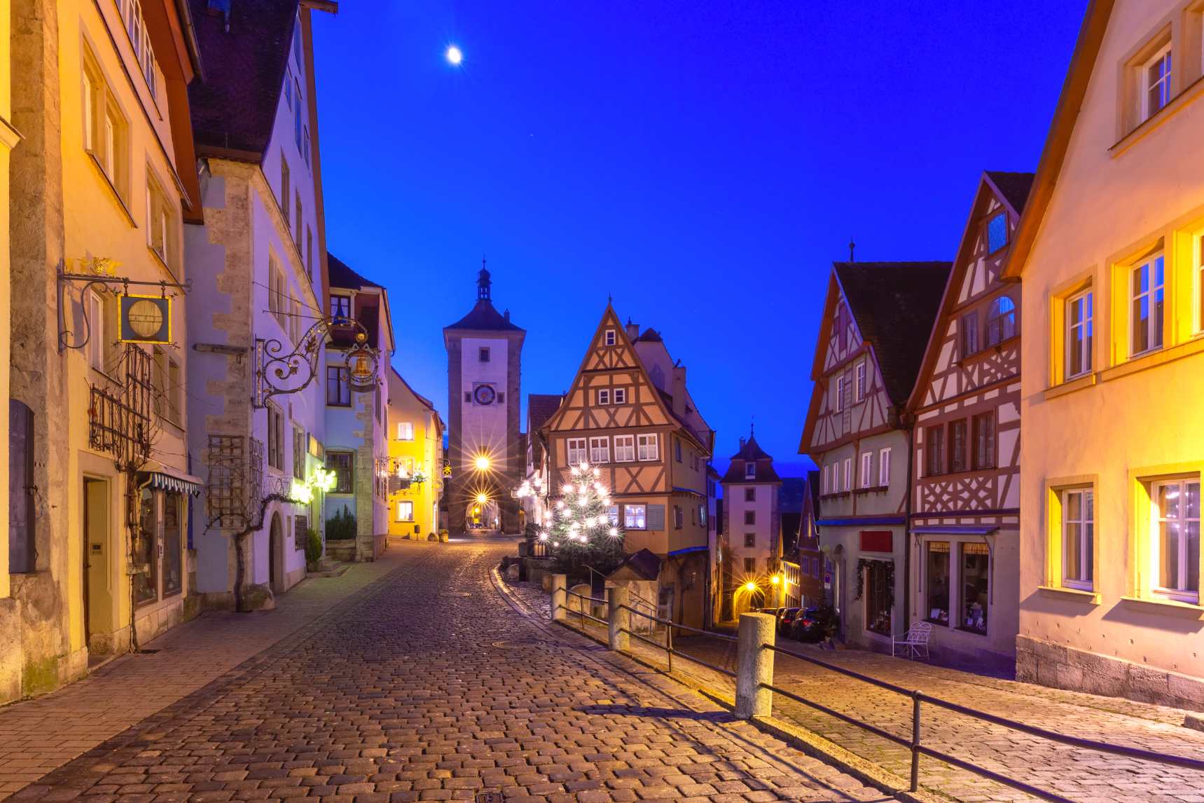Rothenburg ob der Tauber, Germany, at Christmas, featuring illuminated medieval half-timbered houses, cobblestone streets, a decorated Christmas tree, and festive winter lights along the Romantic Road.